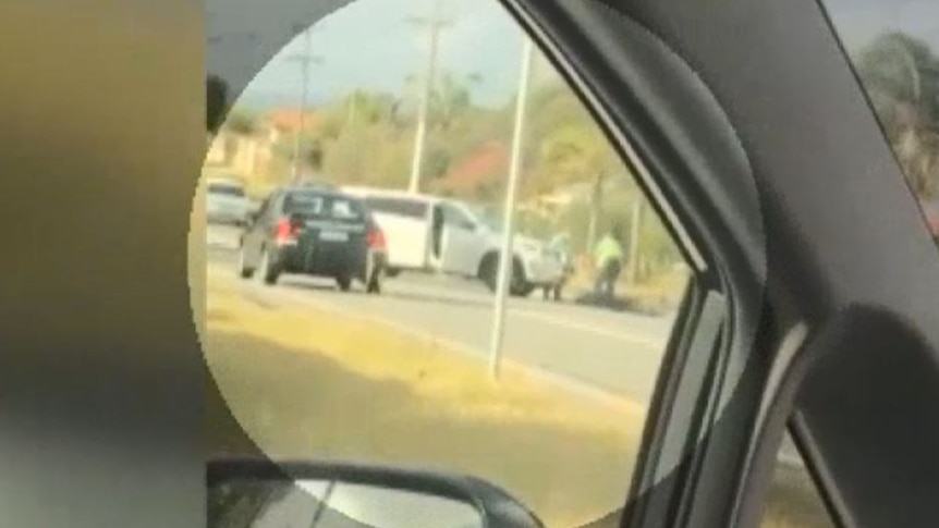 A grainy video of a man lying in front of a white police SUV.