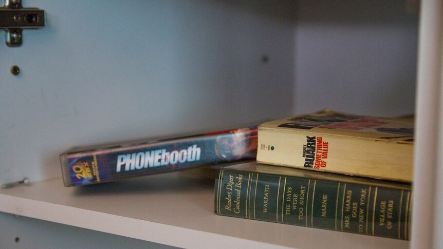 Books and a commercial video cassette on a cupboard shelf.