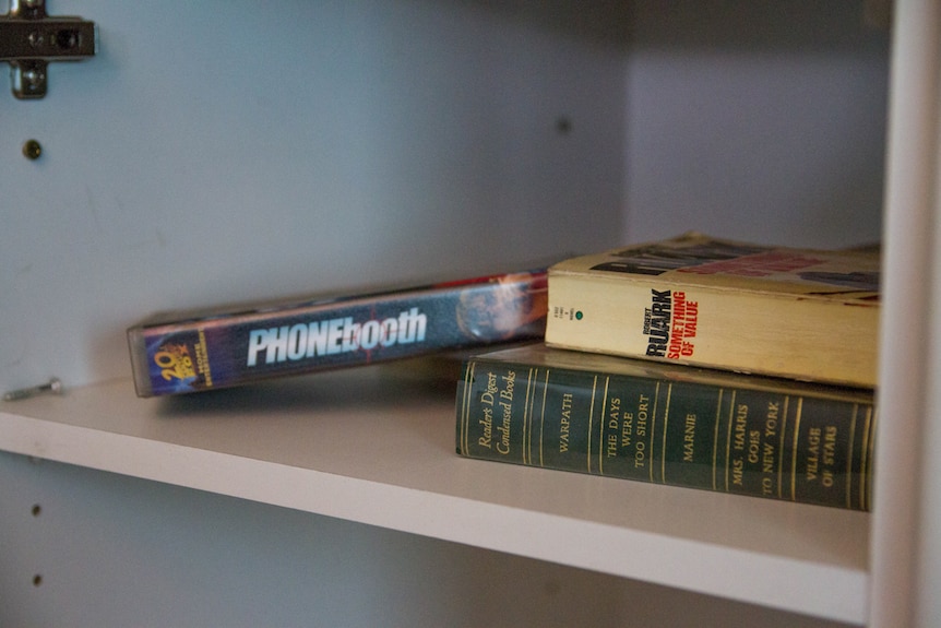 Books and a commercial video cassette on a cupboard shelf.