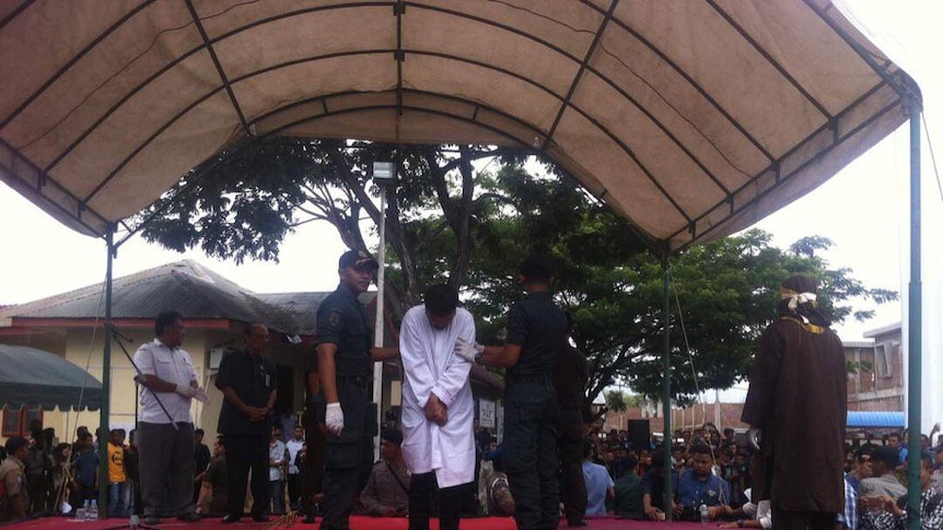 Guards hold a man in place as he stands, bowing his head before being flogged in Aceh, Indonesia.