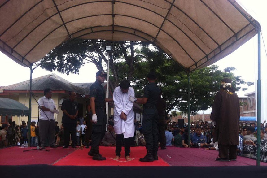 Guards hold a man in place as he stands, bowing his head before being flogged in Aceh, Indonesia.