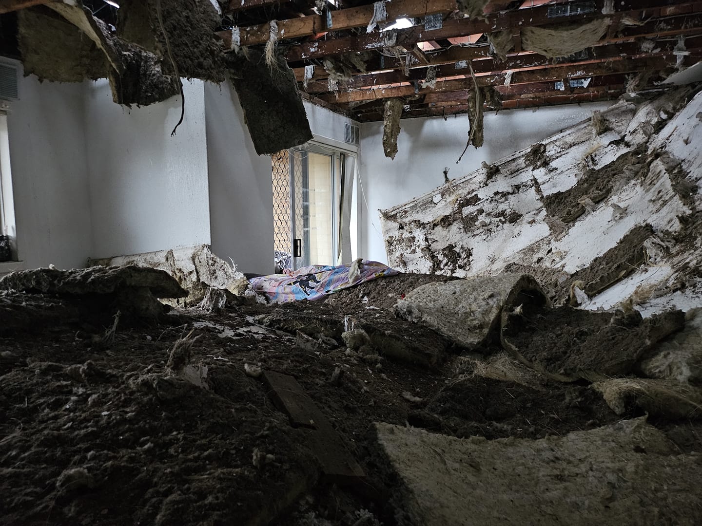 The interior of a house where the the ceiling has fallen through, leaving insulation and drywall piled up.