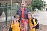 woman stands with little boy and little girl in front of school