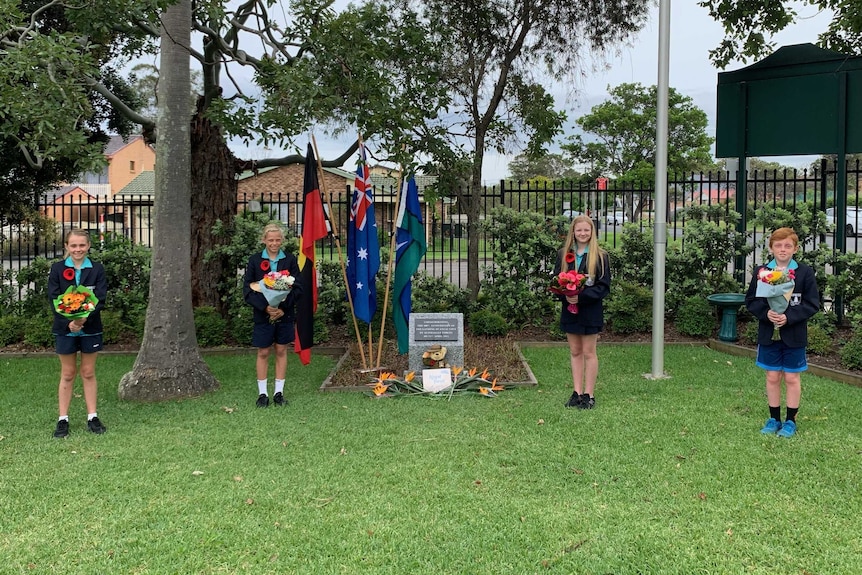 Four school students standing apart at a war memorial.
