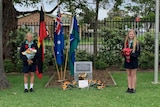 Four school students standing apart at a war memorial.