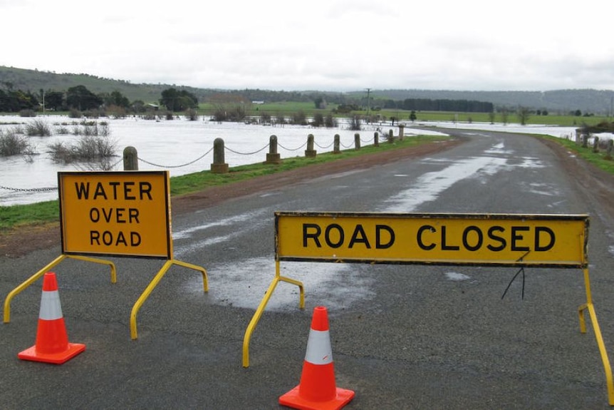 road closed sign across a road. Water off to the side of the road. 