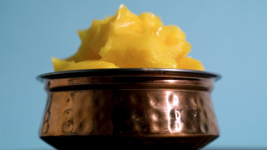 A metal bowl packed with glistening, yellow ghee to depict how to use ghee in cooking.