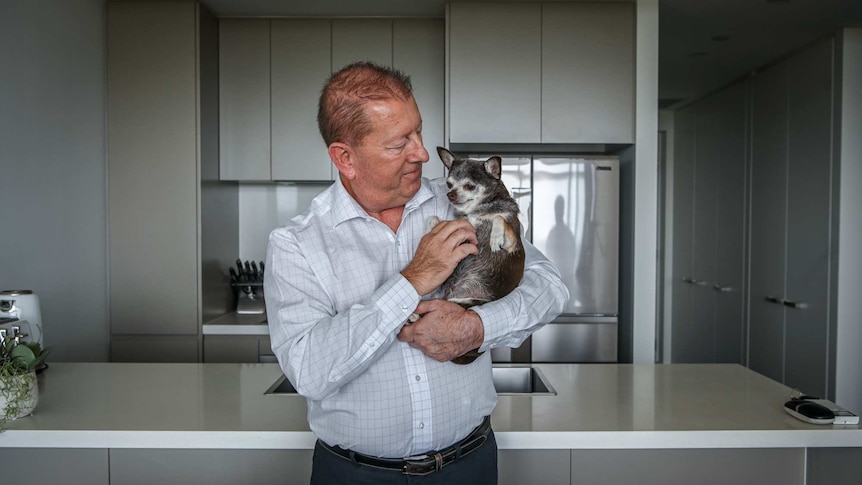 A man cuddles his tiny dog in his kitchen