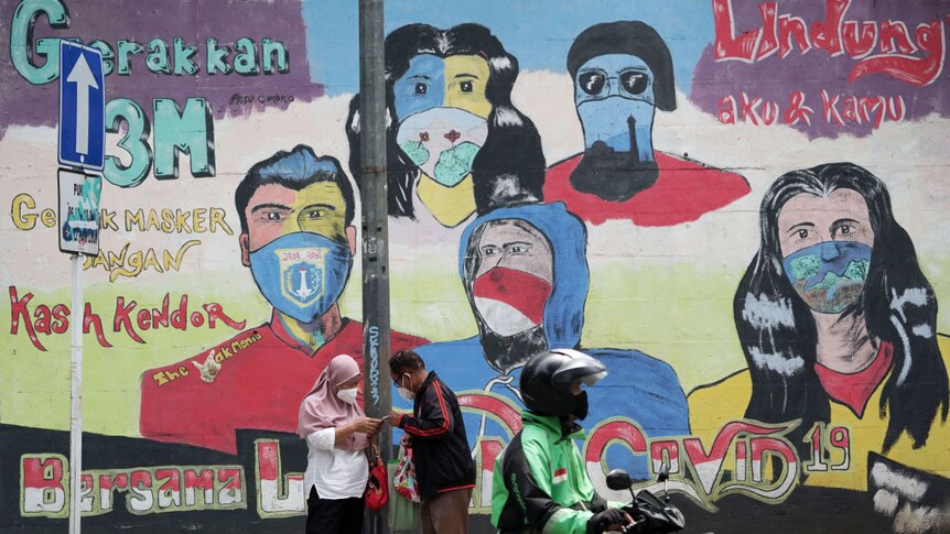 A Gojek rider waits next to a mural in Jakarta, Indonesia.