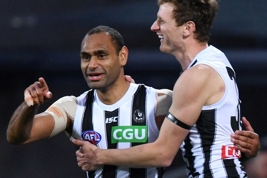Hoskin-Elliott smiles while hugging Varcoe, who is pointing at something off camera.