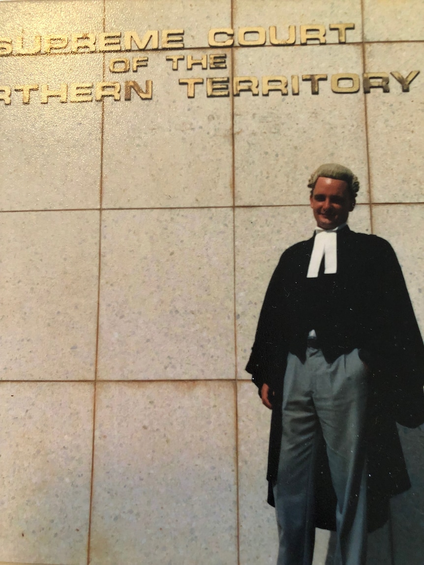 A man in legal wear, including a wig, stands in front of a court building.