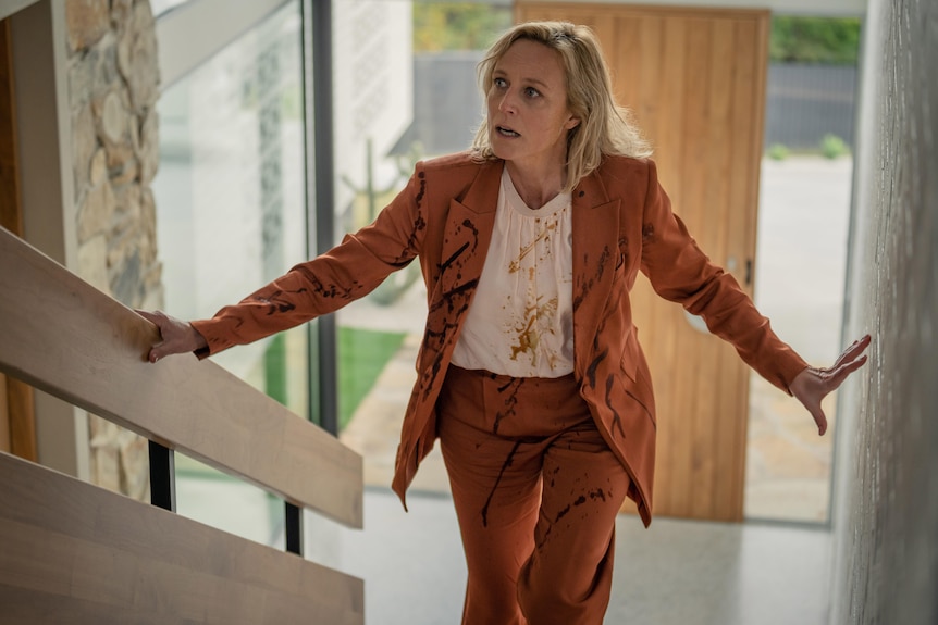 A woman wearing a dirty, orange suit walks up stairs.