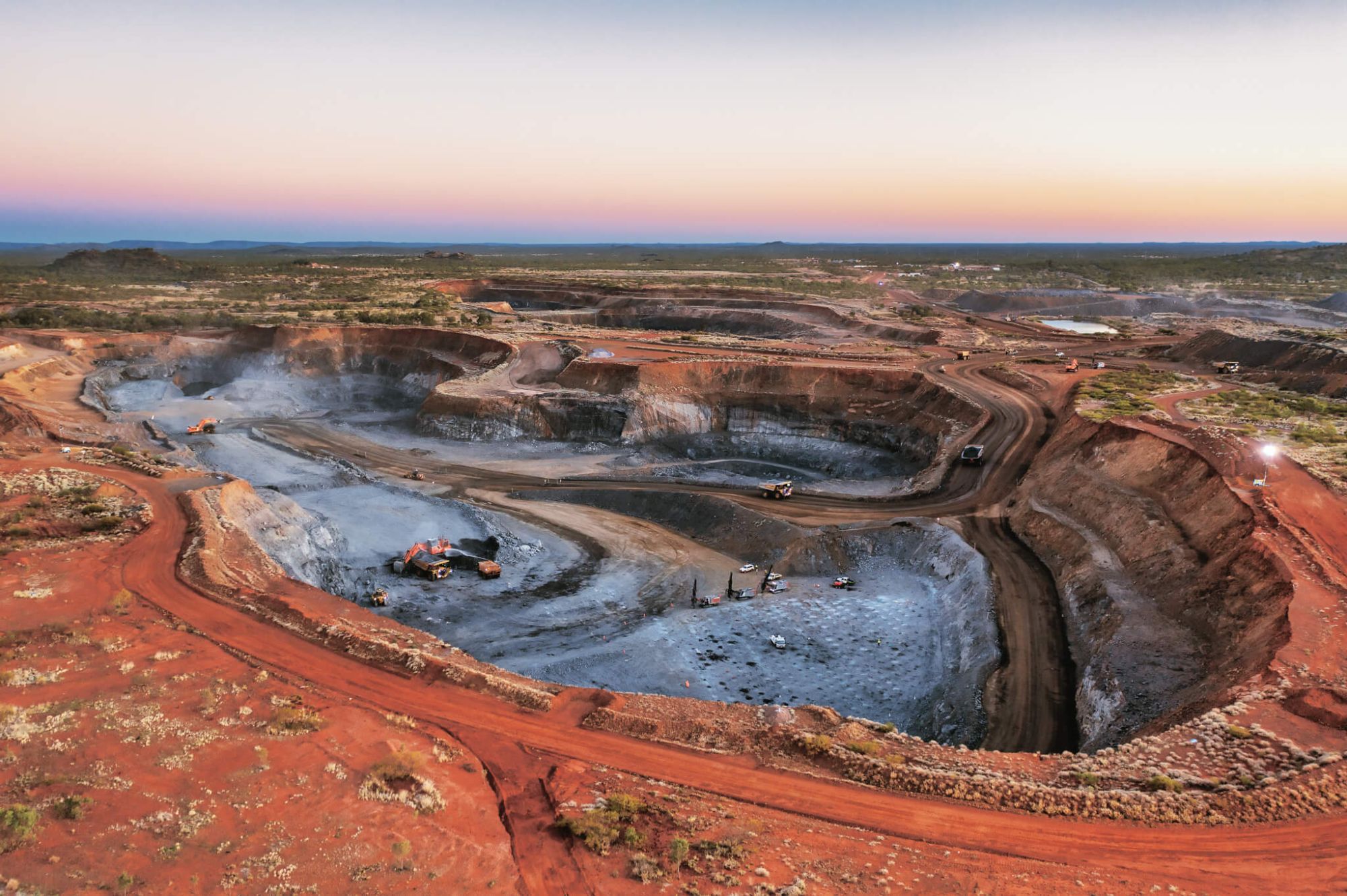 An outback copper mine, a deep pit with machinery in it with red dirt in the background.