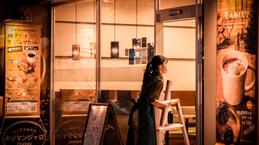 A woman carries a chair into a restaurant at night.