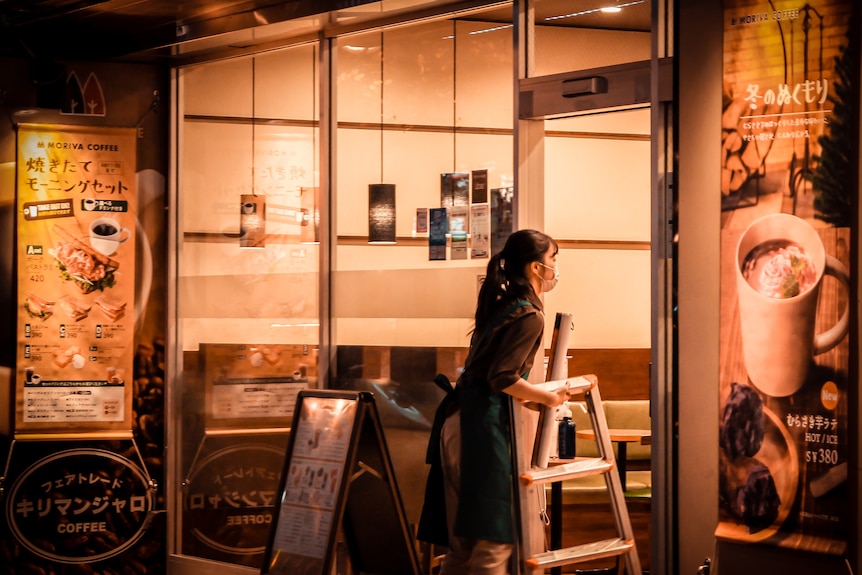 A woman carries a chair into a restaurant at night.