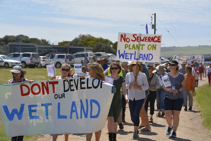 Protesters march carrying signs opposing a development in a wetland.