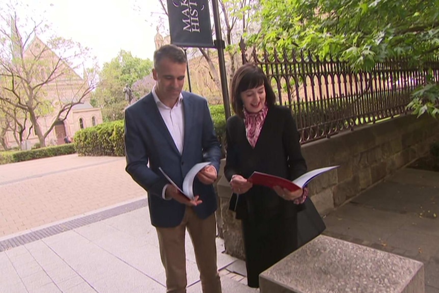 A man and a woman stand next to each other looking over policy booklets in their hands.