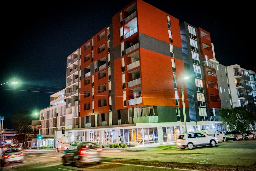Red brick apartment building on a corner of a busy street at night 