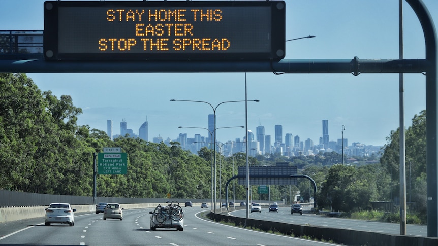 A sign above a highway with a handful of cars on it which reads: "Stay home this Easter. Stop the spread."