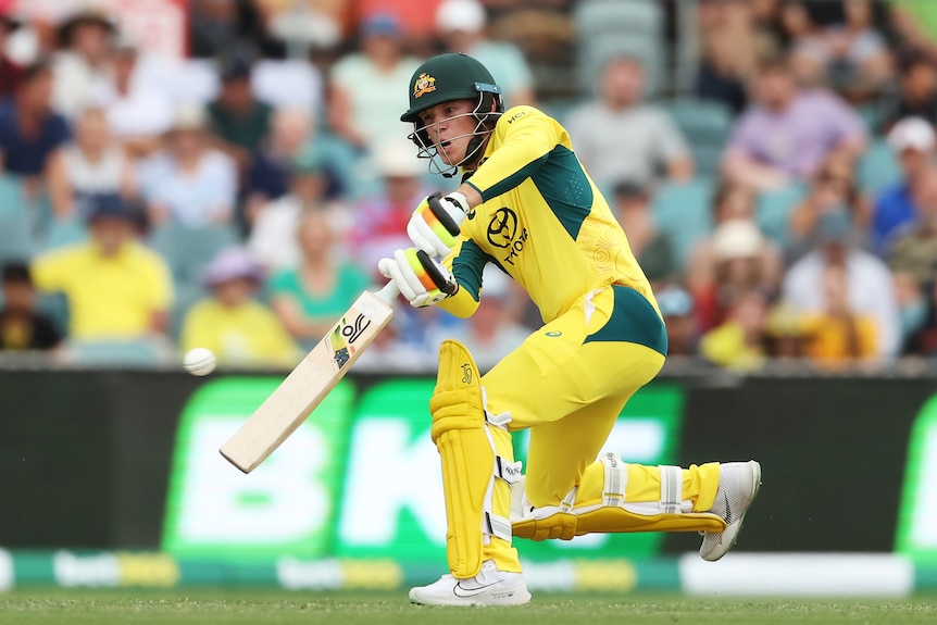 A young Australian batter has his mouth open as he stretches forward and hits down the ground during a one-day international.