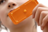 A woman holding a single pill in a bright orange packet.