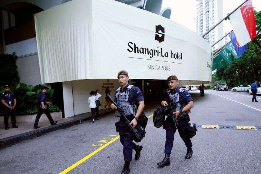 Two armed oficers walk outside entrance to Shangri-La hotel in Singapore