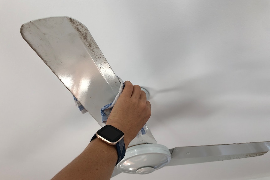 A person's arm holding a cloth, wiping down a dusty ceiling fan