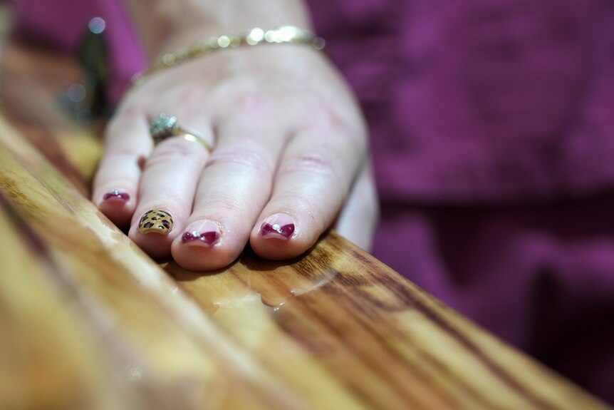 A close up of a hand with painted nails resting on a coffin.