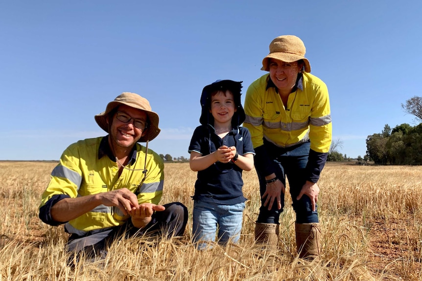 Fair-skinned man and woman wear high-vis shifts, sun-safe hats and long pants. Preschool-aged boy grins in centre amid blue sky