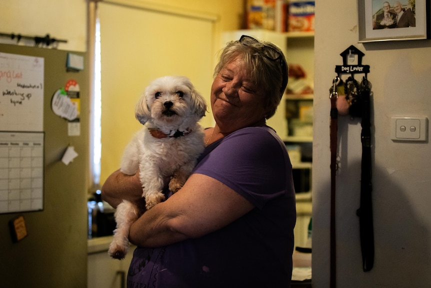 A woman smiles while holding her white dog.