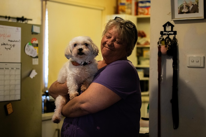 Une femme sourit en tenant son chien blanc.