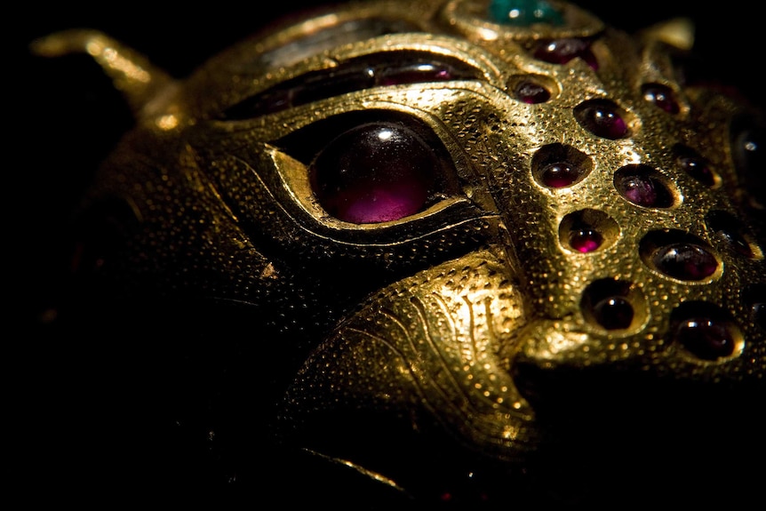 A close up of the face of a gold tiger. Its eyes, stripes and other details are purple gems.