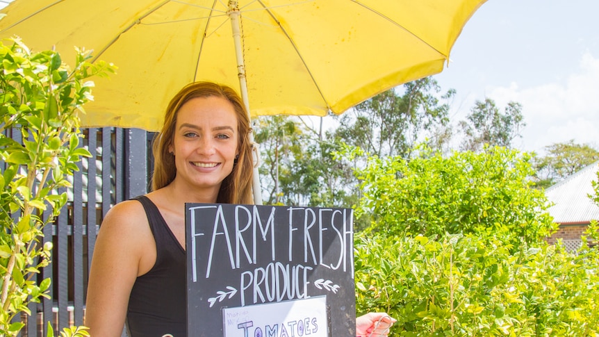 Lady stands under a yellow umbrella with farm produce.