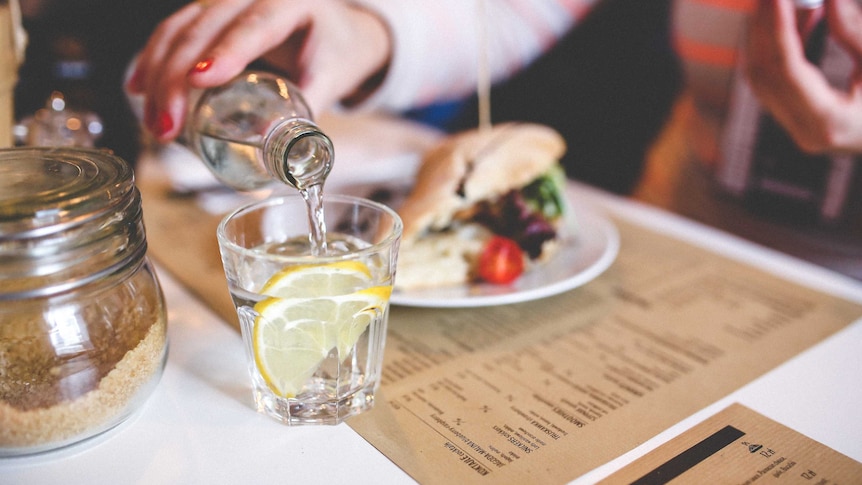 Woman pours glass of water while at a cafe