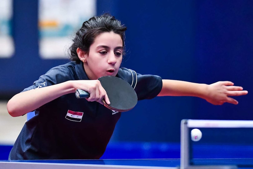A young female table tennis player hits a backhand.