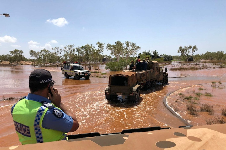 An army truck full of stranded residents drives through flood waters as emergency services watch on.