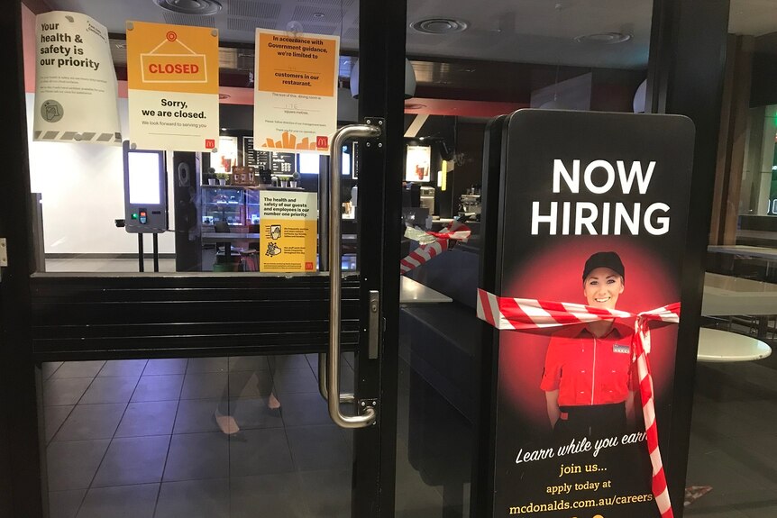 A McDonald's restaurant with a closed sign on the door and red and white tape around a "now hiring" sign.