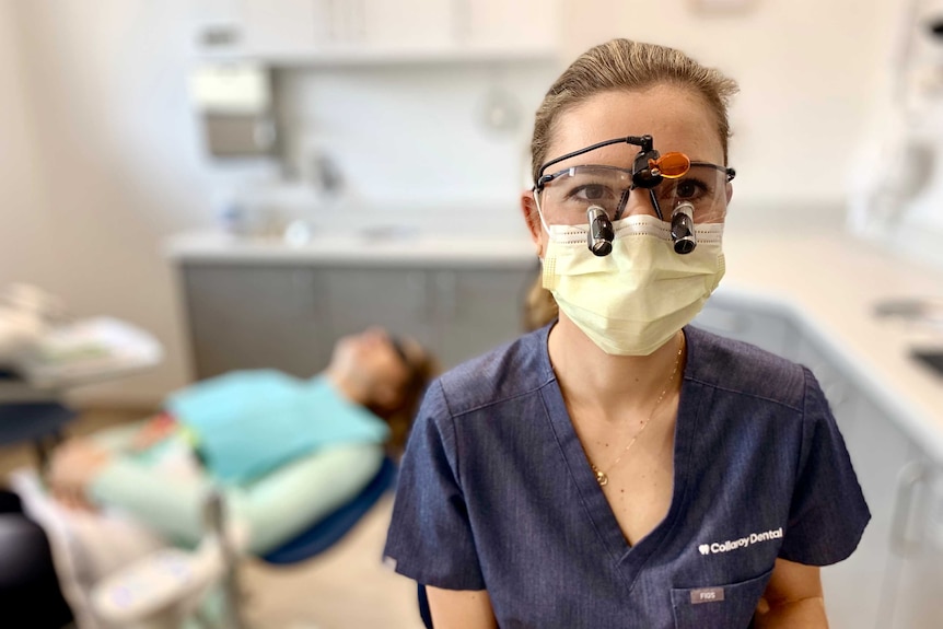 A woman wearing scrubs and dental glasses.