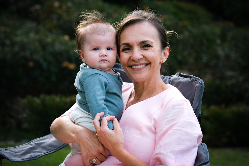 Jasmina, woman in pink shirt smiling, holding a baby wearing a blue shirt.