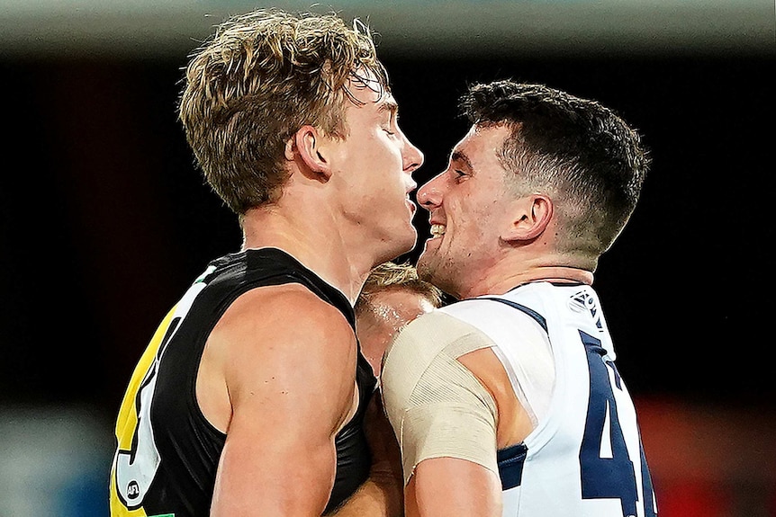 A Richmond AFL player stands only centimetres away from a Geelong opponent as they stare at each other during a confrontation.