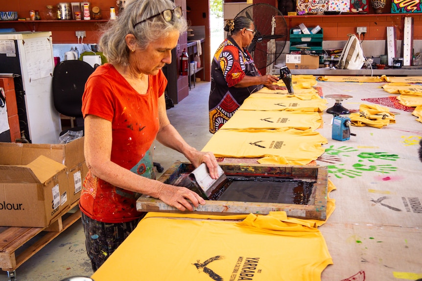 woman screenprinting T-shirts and another woman drying with a hairdrier.