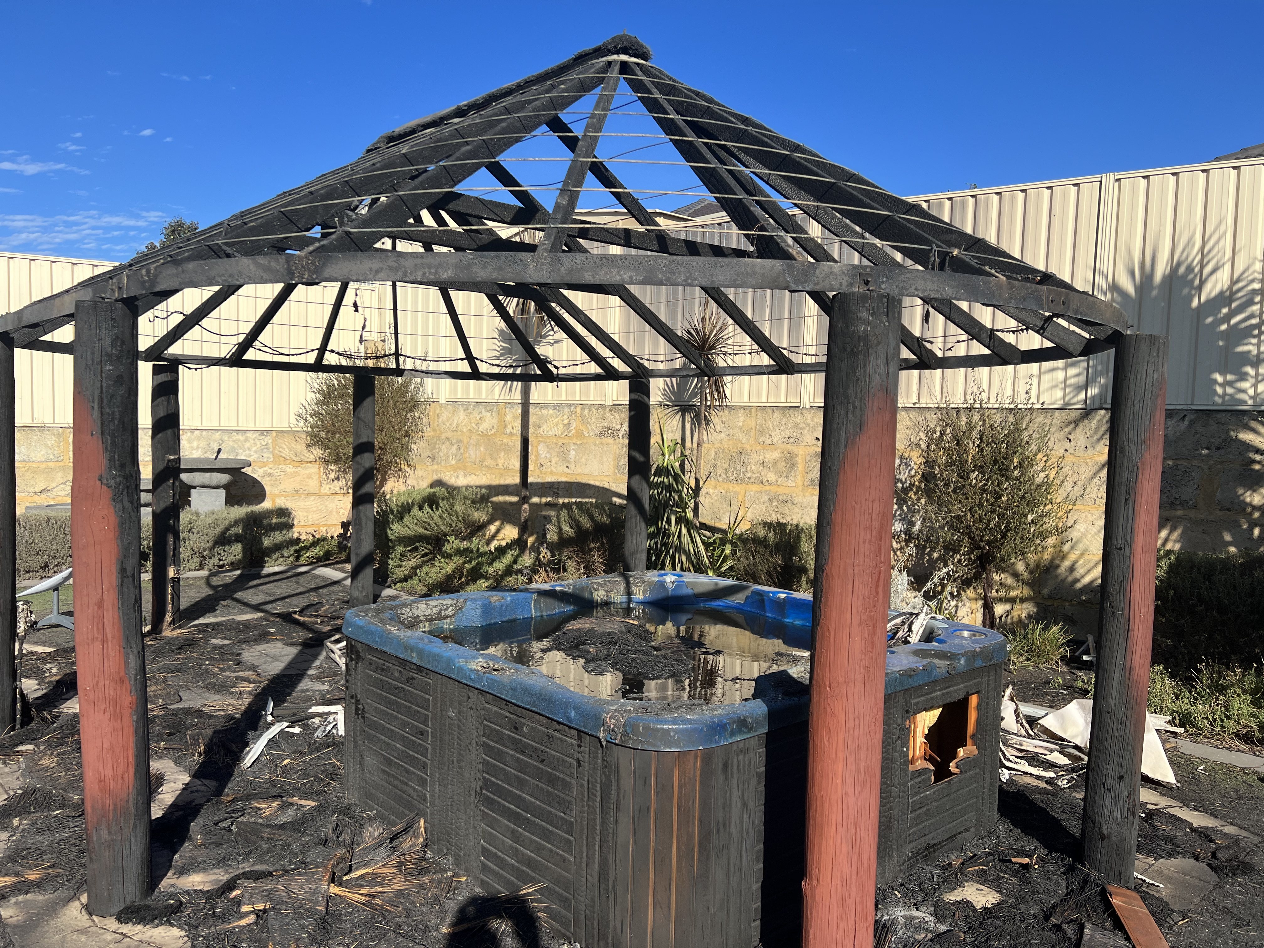 Um gazebo gravemente queimado não tem mais telhado e é exibido acima de um spa queimado