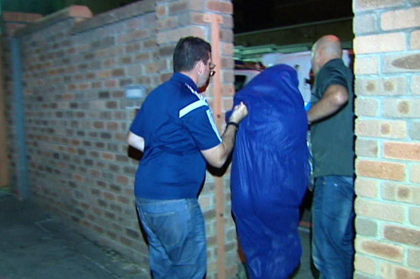 A man wearing a blue jumpsuit is escorted by officers into Curtin House Police station.