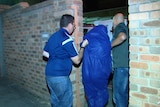 A man wearing a blue jumpsuit is escorted by officers into Curtin House Police station.