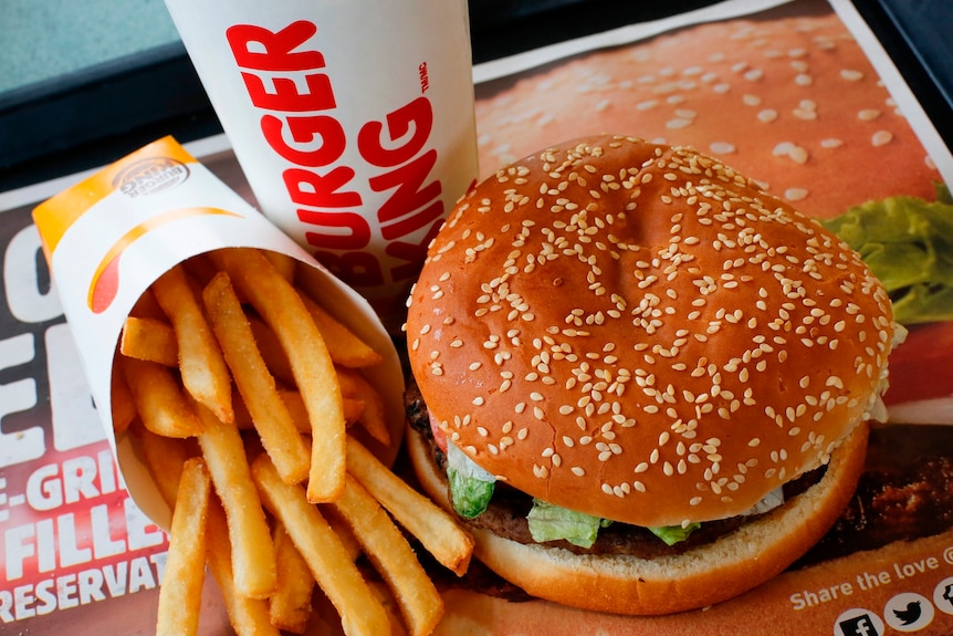 View from above, of a burger in a sesame seed bun, with a packet of fries on its side, and a cup marked Burger King