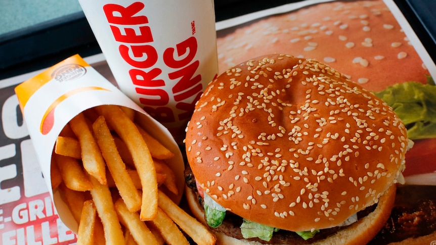 View from above, of a burger in a sesame seed bun, with a packet of fries on its side, and a cup marked Burger King