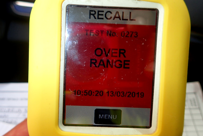 A hand-held breathalyser machine with a display reading "recall over range".