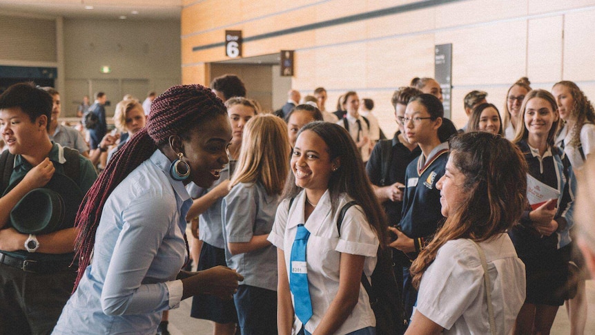 Imaged of a young African woman speaking to a bunch of school students amid a crowded workshop