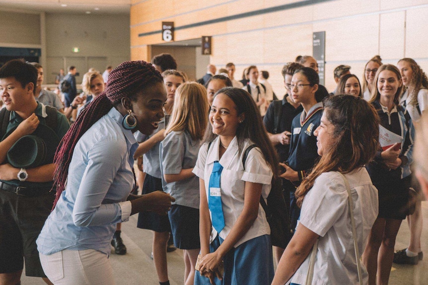 Imaged of a young African woman speaking to a bunch of school students amid a crowded workshop