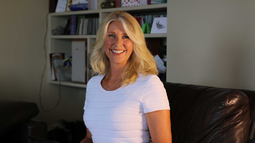 Tracey Spicer smiles on a couch in front of a bookcase